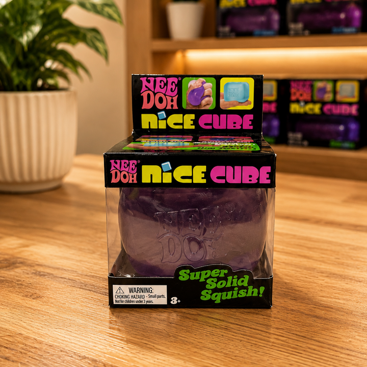 Boxed purple toy labeled 'Nice Cube' on a wooden surface with a plant in the background.